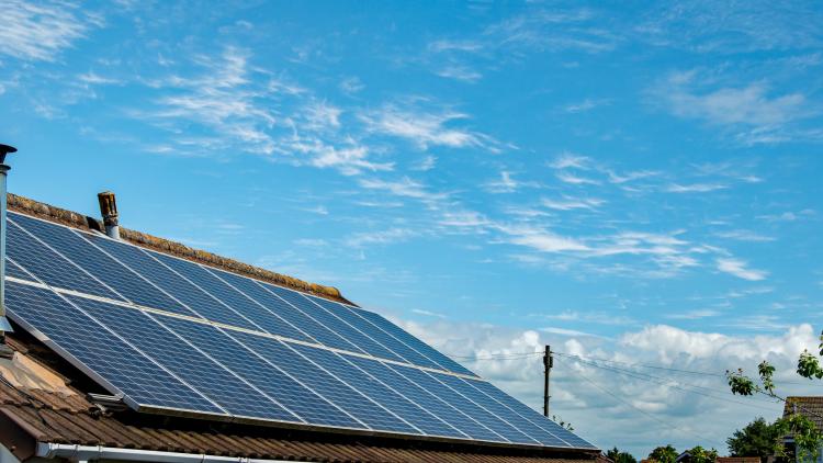 Panoramic image of Solar panels on a domestic house roof with blue sky behind. A sustainable energy image. Good copy space. By Steven